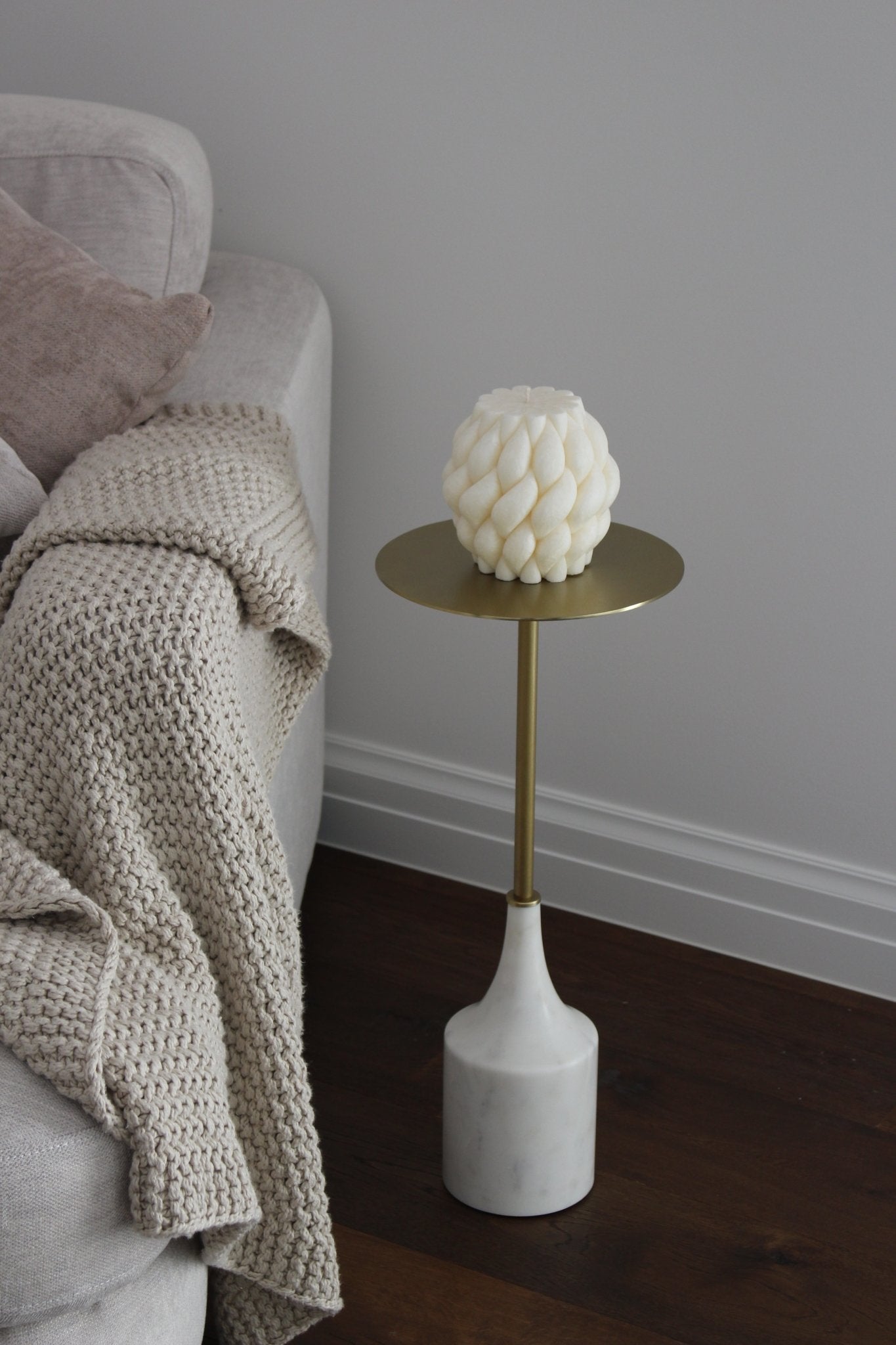 Sculptural Brydie candle in Ivory (white) sitting on a brass and marble side table. This candle has a smooth braid-like exterior similar to a thick knitted wool blanket.