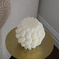 Top view of sculptural Brydie candle in Ivory (white) sitting on a brass and marble side table. This candle has a smooth braid-like exterior similar to a thick knitted wool blanket.