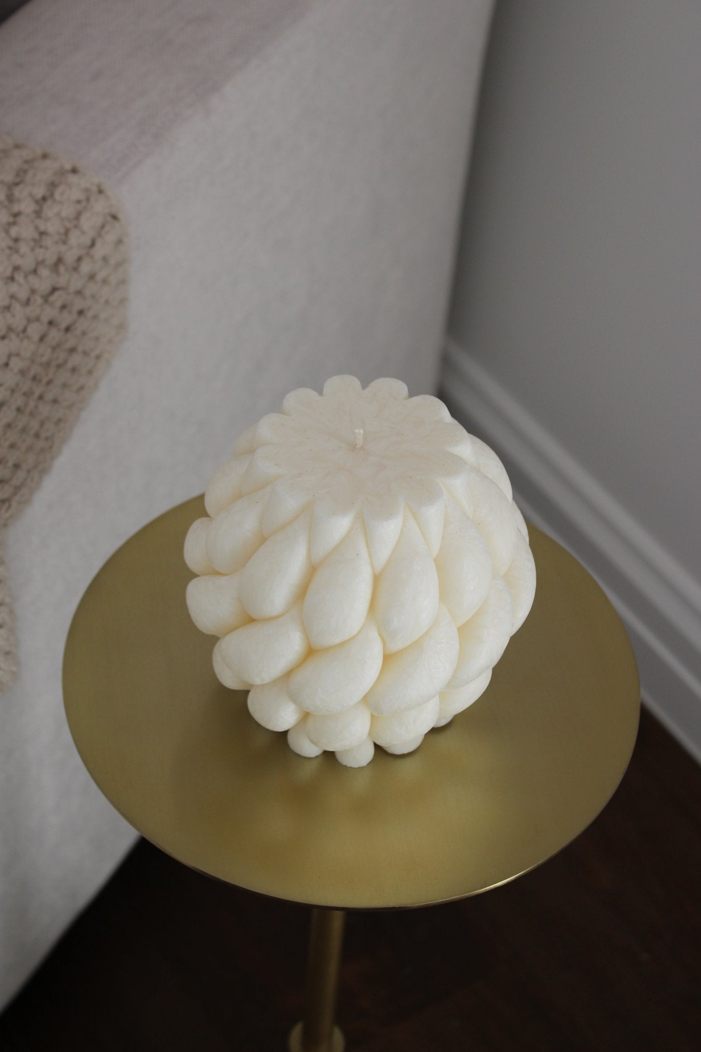 Top view of sculptural Brydie candle in Ivory (white) sitting on a brass and marble side table. This candle has a smooth braid-like exterior similar to a thick knitted wool blanket.