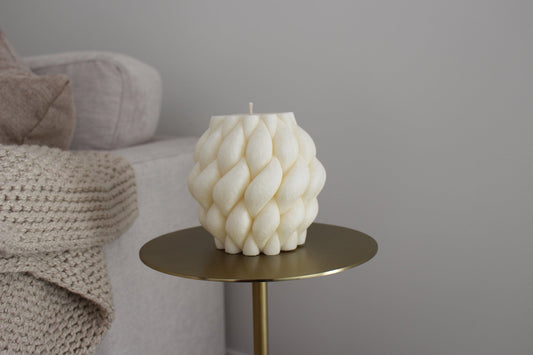 Sculptural Brydie candle in Ivory (white) sitting on a brass and marble side table. This candle has a smooth braid-like exterior similar to a thick knitted wool blanket.