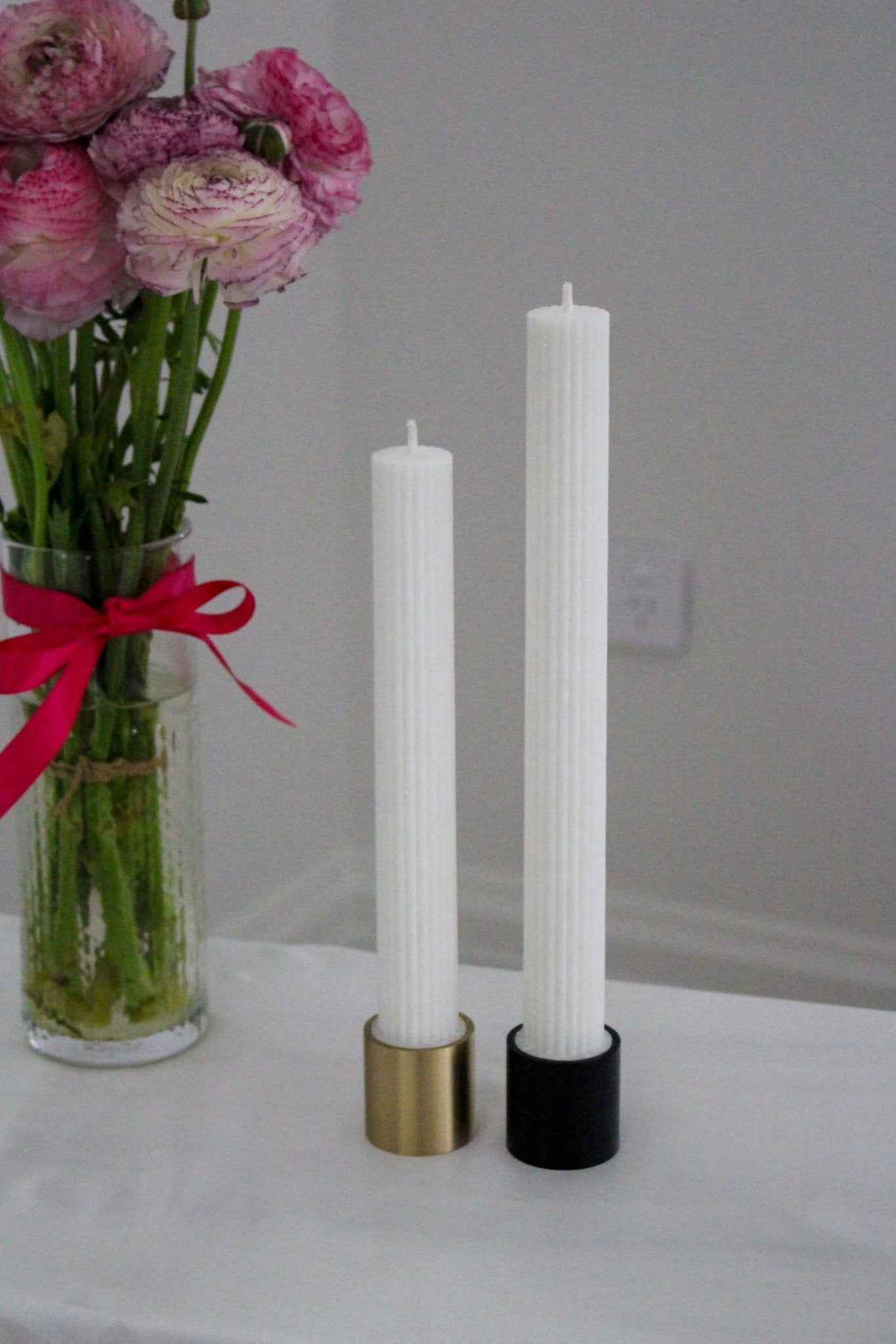 Flat base solid brass gold candlestick holder and brass black candlestick holder shown. Candles are positioned in each candle holder.