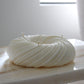 Sculptural round and curvy Lola candle in Ivory (white) colour positioned on a marble side table. Side view shown.