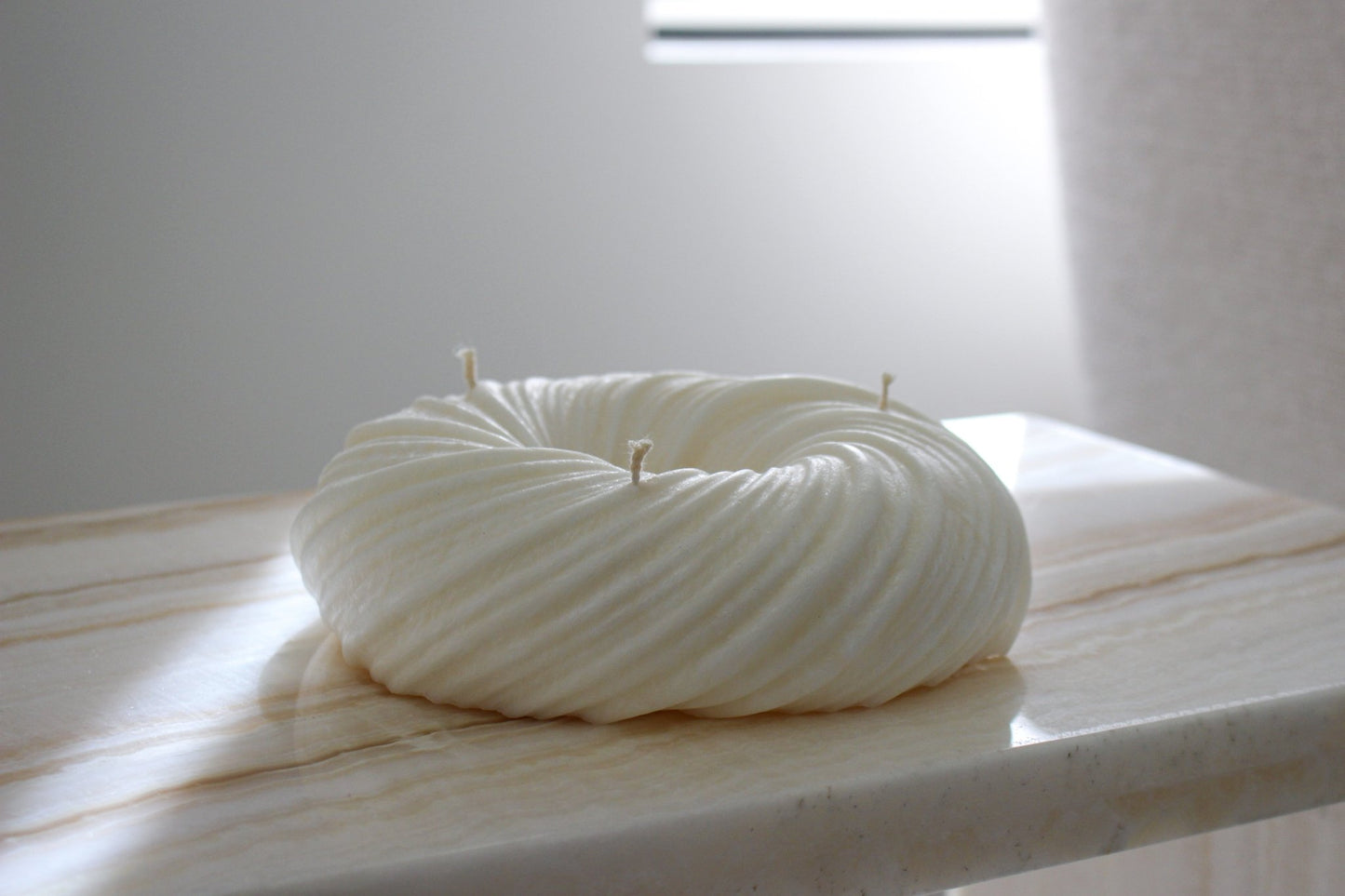 Sculptural round and curvy Lola candle in Ivory (white) colour positioned on a marble side table. Side view shown.