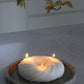 Sculptural round and curvy Lola candle in Ivory (white) colour positioned on a marble tray. The candle is lit in a dim setting.