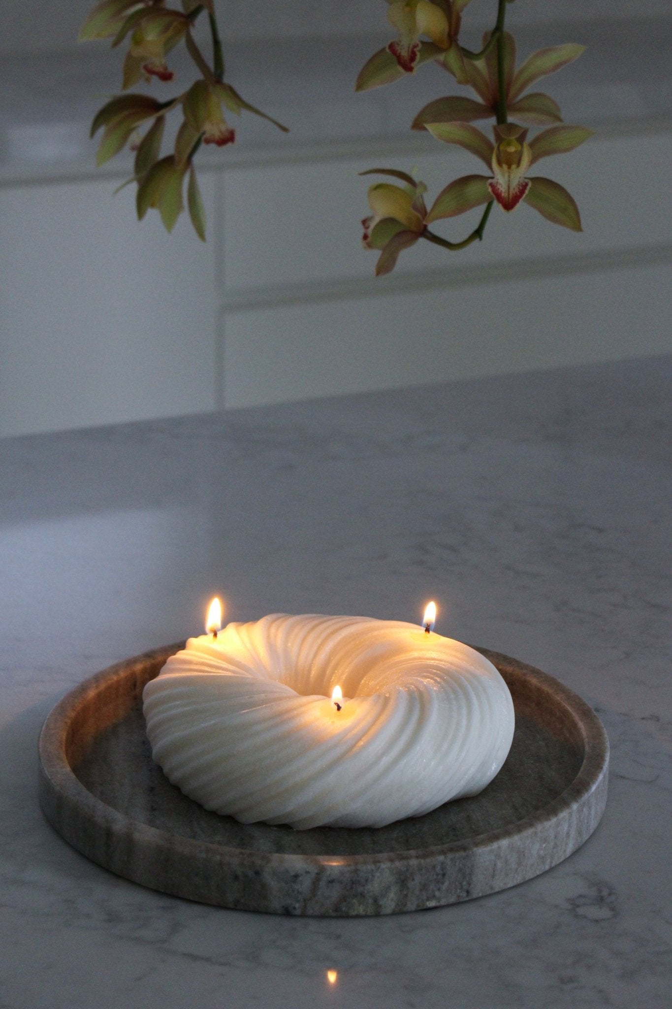 Sculptural round and curvy Lola candle in Ivory (white) colour positioned on a marble tray. The candle is lit in a dim setting.