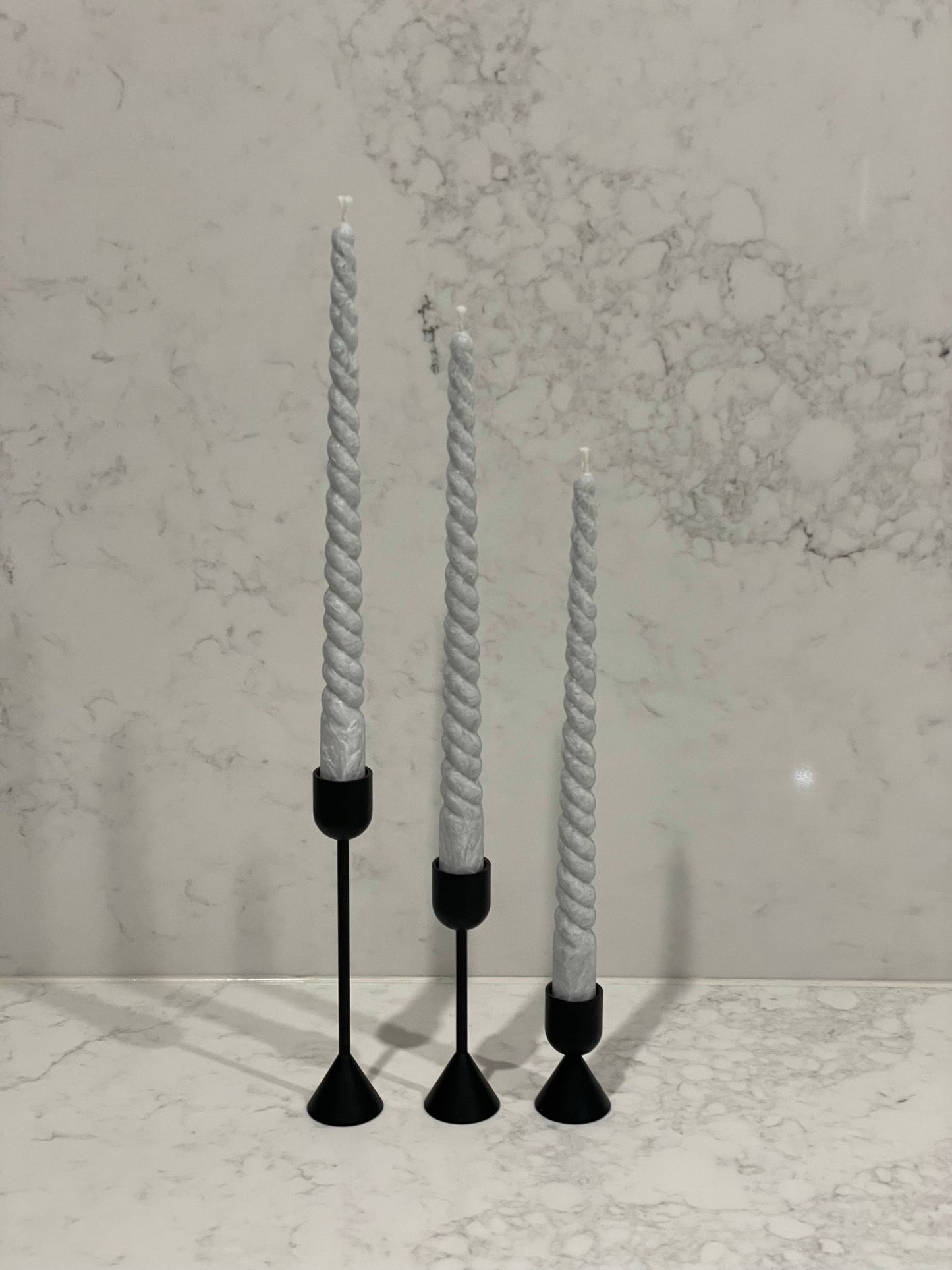 Two sided solid brass black candlestick holders. Set of 3 holders shown with grey taper candles in them positioned on a marble table.