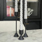 Two sided solid brass black candlestick holders. Set of 3 holders shown with grey taper candles in them positioned on a marble table.
