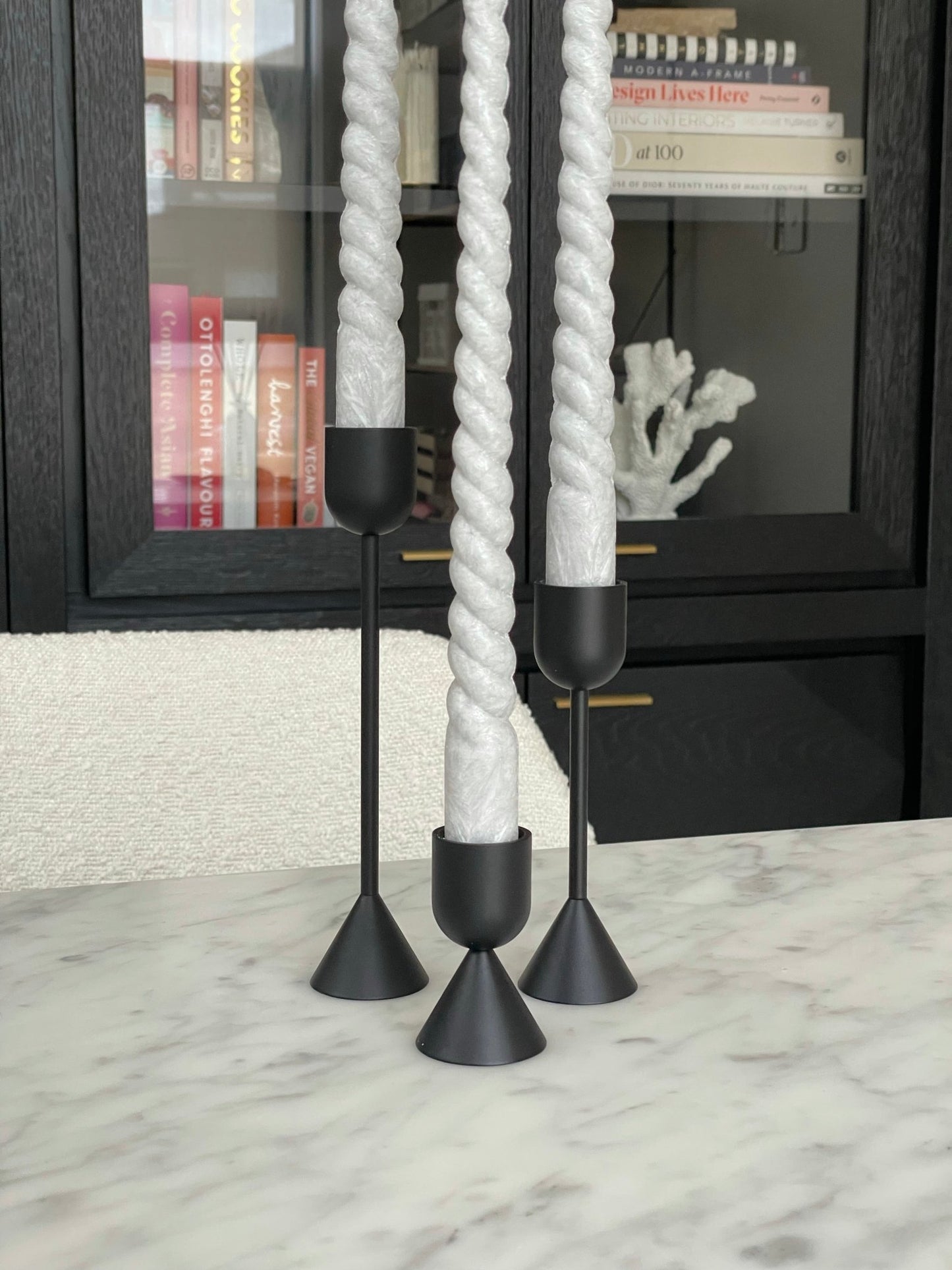 Two sided solid brass black candlestick holders. Set of 3 holders shown with grey taper candles in them positioned on a marble table.