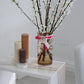 Arrangement of fluted pillar candles shown in white onyx (cream, caramel and cacao (chocolate brown) colours positioned on a side table near a vase of flowers.